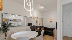 A modern living room with a white dining table, a black leather sofa, and a large mirror. - Downtown Setúbal Apartment (Setúbal)