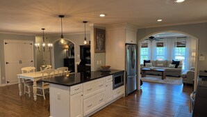 Una cocina amplia con una isla central, muebles blancos e iluminación colgante.