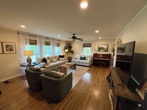 A spacious living room with a large flat-screen TV, a piano, and a ceiling fan. - Charming 3 bedroom Masters rental, less than 2 miles from Augusta Nationals! (Augusta)