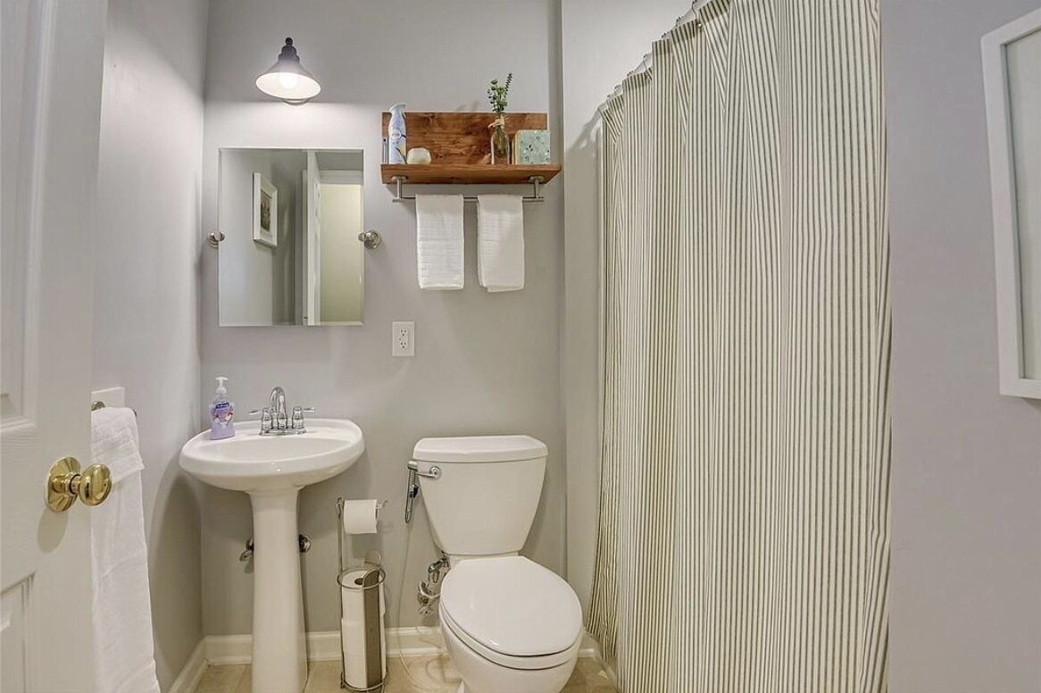 A bathroom with a pedestal sink, toilet, and a wooden shelf above the sink.