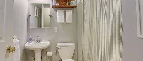 A bathroom with a pedestal sink, toilet, and a wooden shelf above the sink.