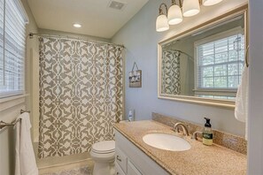A bathroom with a patterned shower curtain, a large mirror, a sink with a soap dispenser, and a towel rack. - Charming 3 bedroom Masters rental, less than 2 miles from Augusta Nationals! (Augusta)