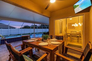Un patio al aire libre con una mesa de comedor para cuatro personas, una piscina y un área de estar cubierta.