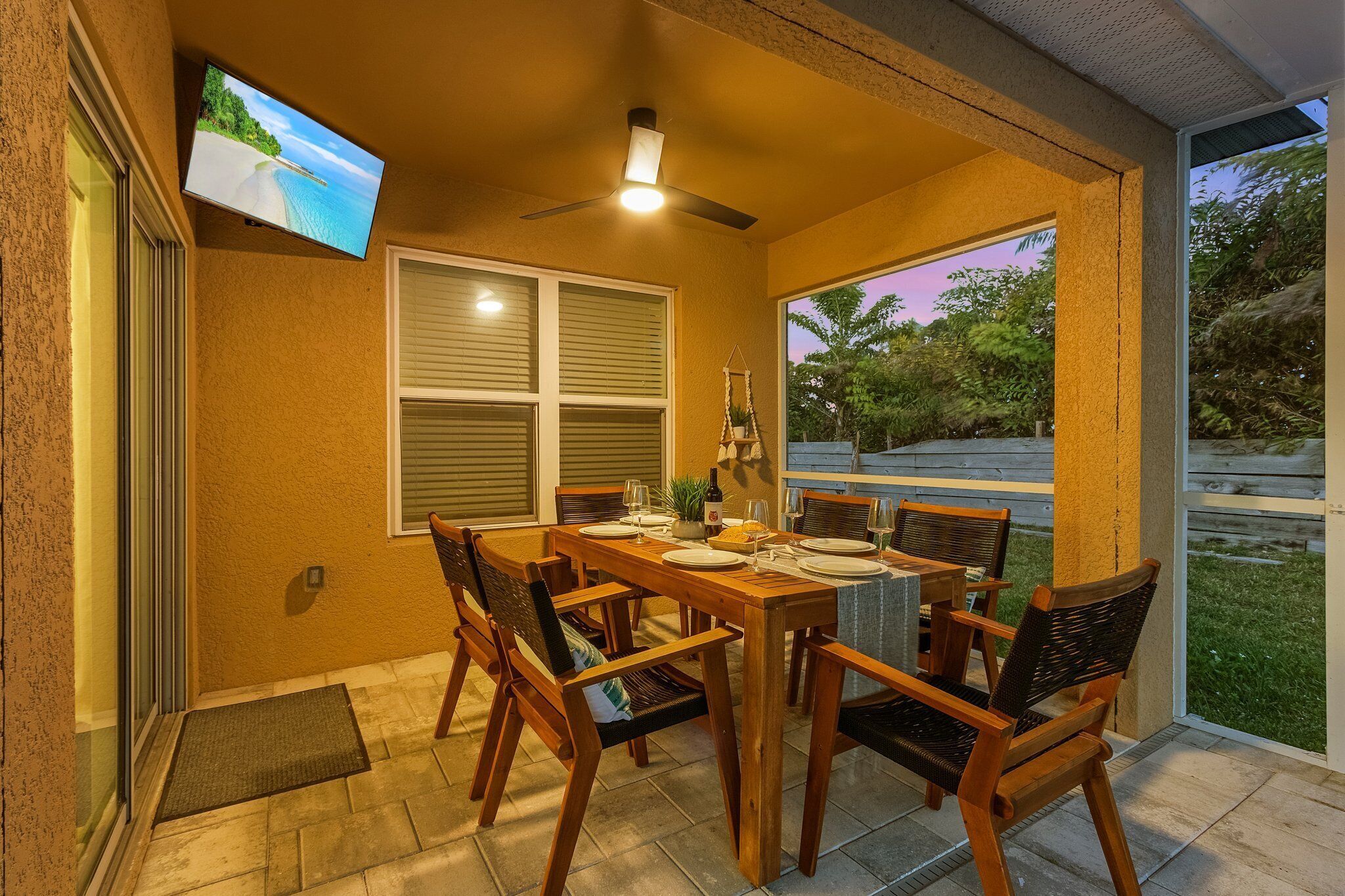 Een overdekt terras met een eettafel voor vier personen, een plafondventilator en een aan de muur bevestigde televisie.