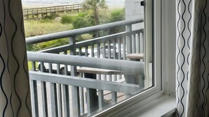 En balkon med gelænder i hvidt, udsigt over en græsplæne og en overskyet himmel.