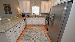 A kitchen with white cabinets, granite countertops, a stainless steel refrigerator, and a patterned rug. - Sea For Yourself - 1/2 Block to Ocean in Surfside Beach (Surfside Beach)
