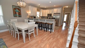A spacious kitchen with white cabinetry, a central island with stools, and a wooden staircase. - Sea For Yourself - 1/2 Block to Ocean in Surfside Beach (Surfside Beach)