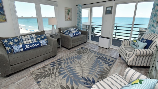 A spacious living room with a view of the ocean, furnished with a sofa, armchair, and a patterned rug. - Carolina Shores II 1404 - Oceanfront Complex in Garden City Beach (Garden City Beach)