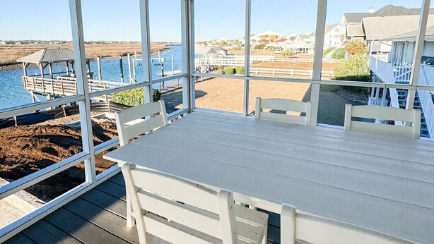 A covered outdoor area with a table and chairs, overlooking a beach and water. - Inlet Holiday - Creekfront in Garden City Beach (Garden City Beach)