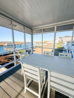 Un espace extérieur abrité, doté d’une table et de chaises, offrant une vue sur une plage et l’océan.