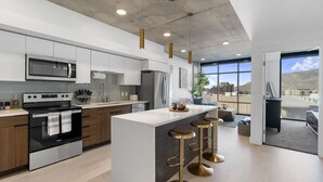 A modern kitchen with a central island, stainless steel appliances, and a large window offering a view of the city. - Perfect Dntwn Retreat- Convention Cntr- Amenities! (Salt Lake City)