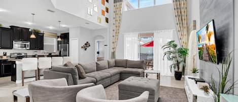 A spacious living area with a large sectional sofa, a dining table, and a kitchen in the background.