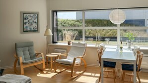 A room with a large window, a dining table with chairs, a rocking chair, and a framed picture on the wall. - 2 bedroom stunning apartment in Fanø (Fanø)