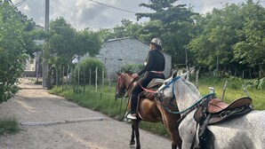 A person riding a horse on a dirt path with a white building and greenery in the background. - Punta Arena EcoHostal & EcoFit (Cartagena)