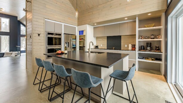 A modern kitchen with a central island, bar stools, built-in appliances, and open shelving. - The Experience SÔ Lodge (SHEFFORD)