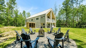 A two-story house with a large porch and outdoor seating area with Adirondack chairs. - The Experience SÔ Lodge (SHEFFORD)