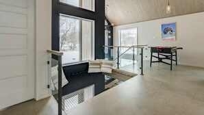 A modern interior with a staircase leading to a loft area, large windows, and a foosball table. - The Experience SÔ Lodge (SHEFFORD)