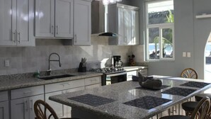 A modern kitchen with granite countertops, white cabinets, a gas stove, and a large window offering a view of the outdoors.