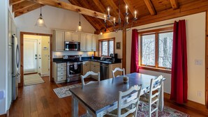 Una cocina acogedora con vigas de madera, un comedor con mesa y sillas, y vistas a árboles a través de una ventana.