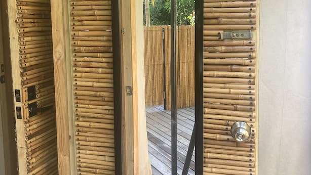 Una habitación con pared de bambú y puerta con manija de metal.