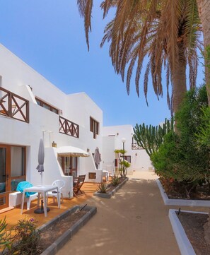 A courtyard with white buildings, outdoor seating, and palm trees.