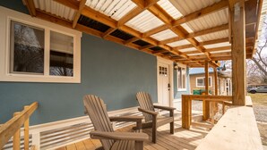 A covered wooden deck with Adirondack chairs, a wooden table, and a view of a house with a blue exterior. - Modern Bungalow in the Heart of Fruita (Fruita)
