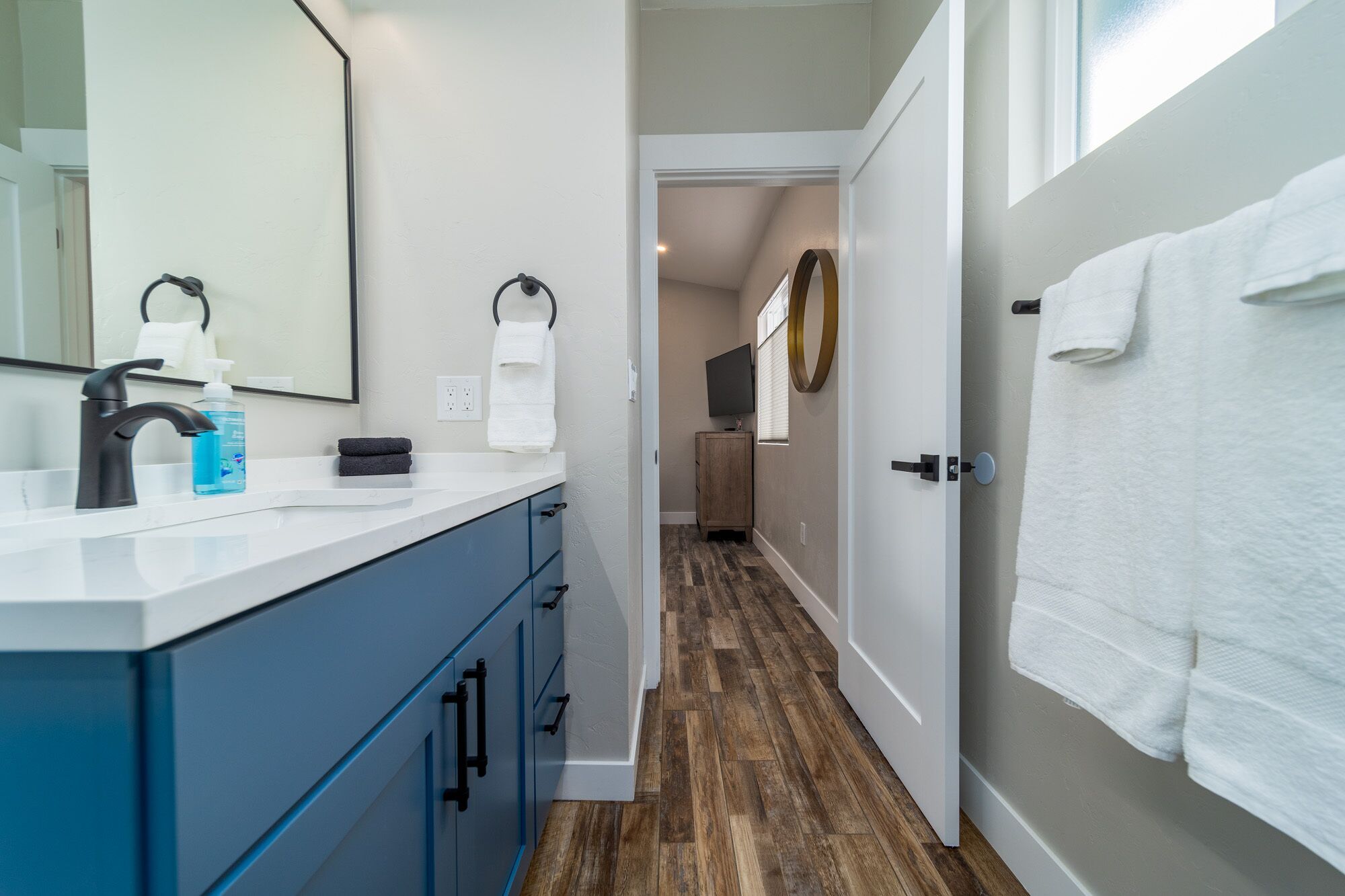 A modern bathroom with a white sink, dark blue cabinets, and a wooden floor.