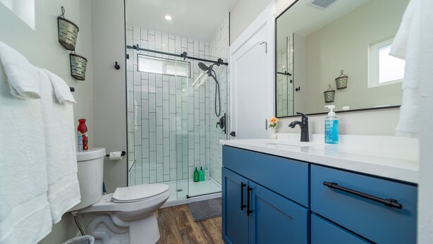 Une salle de bain moderne avec une douche à parois de verre, des toilettes blanches et un meuble-lavabo bleu avec un miroir.