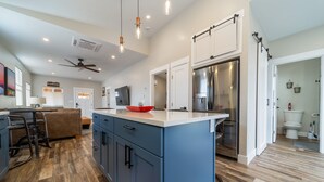 A modern kitchen with blue cabinets, a stainless steel refrigerator, and a wooden floor. - Modern Bungalow in the Heart of Fruita (Fruita)