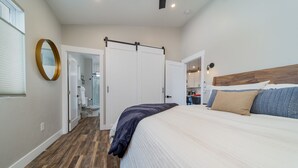 A bedroom with a bed, a wooden headboard, a wardrobe, and a bathroom visible through an open door. - Modern Bungalow in the Heart of Fruita (Fruita)