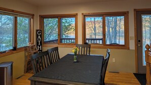 A dining area with a table, chairs, and a view of trees through large windows. - Lake Home property (Luck)