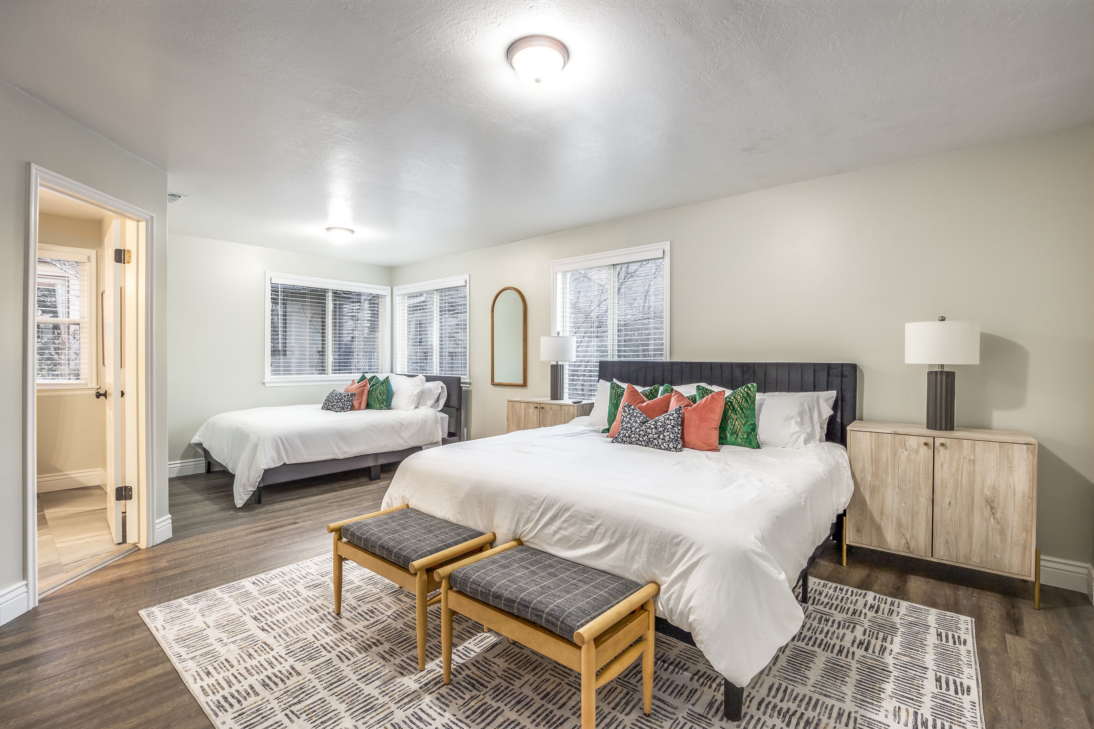 A bedroom with two beds, a wooden bench, a cabinet, and a window with blinds.