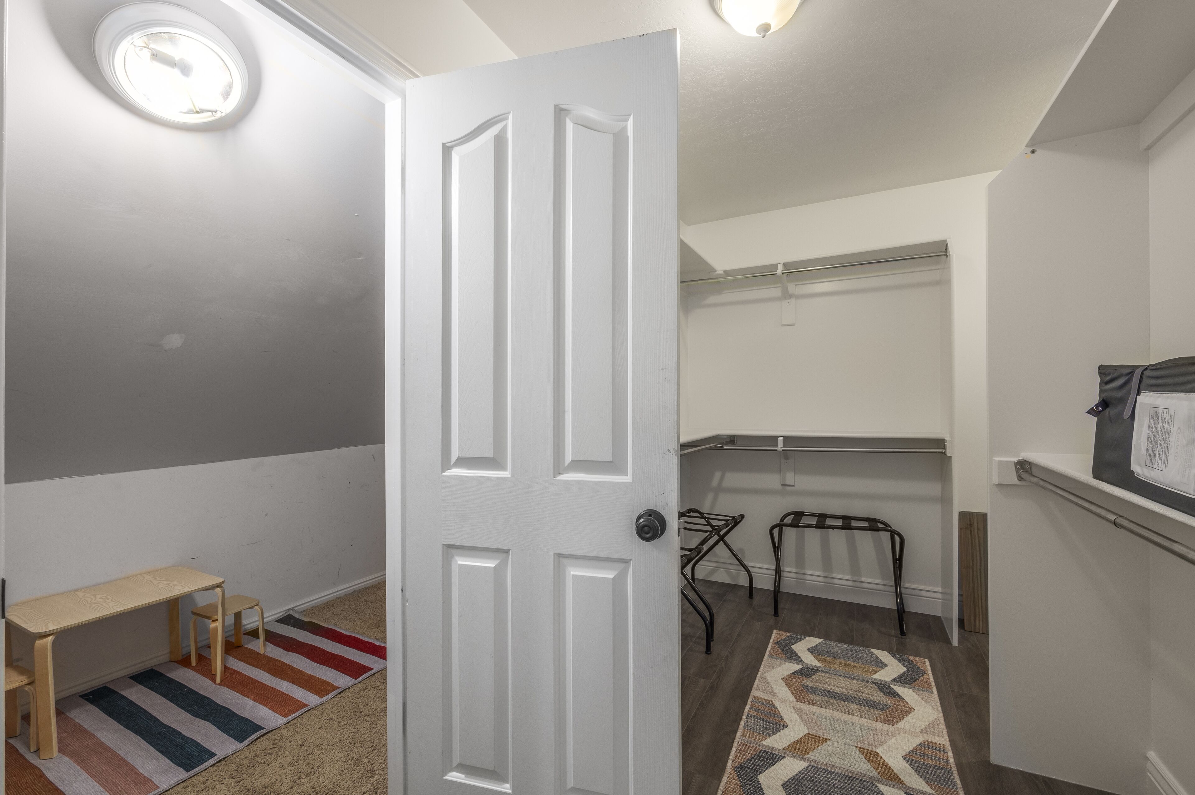 A hallway with a white door, a small table, a bench, and a patterned rug.