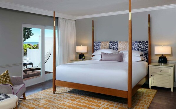 A four-poster bed with a patterned headboard, bedside tables with lamps, a view of the outdoors, and a chair with a cushion.