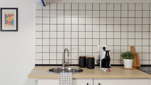 A kitchen with a stainless steel sink, two black mugs, a white kettle, a potted plant, and a wooden cutting board on the counter. - Ghiberti - Loft in the city center (Trieste)