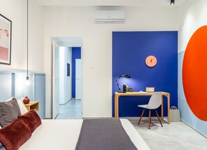 A modern bedroom with a bed, bedside table, and a desk with a chair. There is a clock on the wall and an air conditioning unit above the desk. - Ghiberti - Loft in the city center (Trieste)