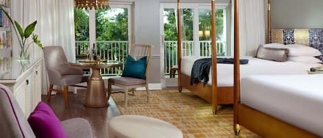 Une chambre d’hôtel dotée d’un lit à baldaquin, d’un coin salon avec une table et des chaises, et d’un balcon offrant une vue sur la verdure.
