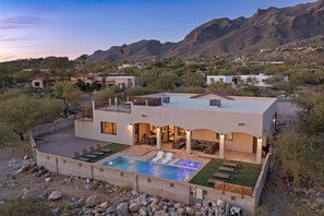 Une maison moderne à deux étages, dotée d’une piscine, d’un espace extérieur aménagé et offrant une vue sur les montagnes.