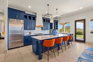 Uma cozinha moderna com armários azul-escuros, eletrodomésticos de aço inoxidável e uma ilha central com banquetas.