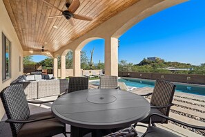 Um pátio ao ar livre com mesa e cadeiras redondas, piscina e vista para uma paisagem montanhosa.