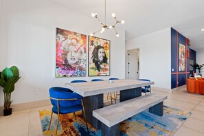 Uma área de jantar moderna com uma mesa grande, cadeiras azuis e obras de arte vibrantes nas paredes.