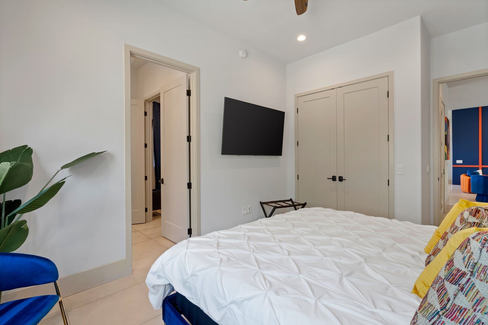 A bedroom with a bed, a TV mounted on the wall, a wardrobe, and a plant.