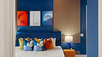 Ein modernes Schlafzimmer mit blauer Akzentwand, einem gepolsterten Kopfteil und einem Nachttisch mit Lampe.