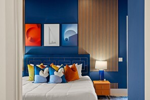 Ein modernes Schlafzimmer mit blauer Akzentwand, einem gepolsterten Kopfteil und einem Nachttisch mit Lampe.