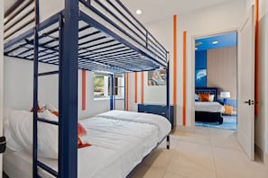 A hotel room with a bunk bed, a desk, a chair, and a window.