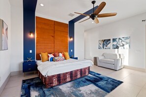 Quarto moderno com cama grande, ventilador de teto e sofá branco.
