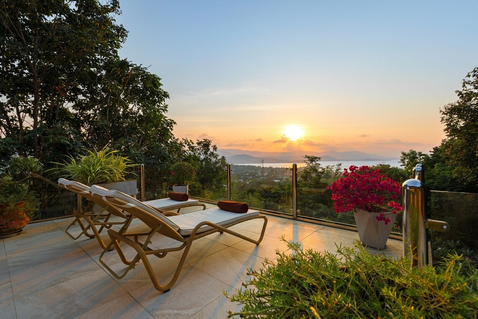 A terrace with wicker lounge chairs and a view of the sunset over a body of water.