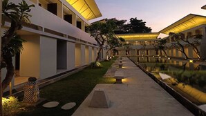 A modern hotel with a central courtyard, featuring a reflective pool and a pathway lined with benches. - Kuta Living (Kuta)