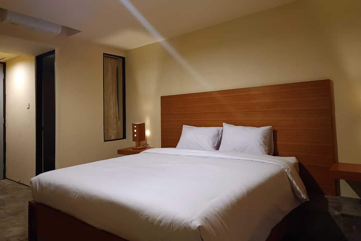 A neatly made bed with a wooden headboard in a hotel room.
