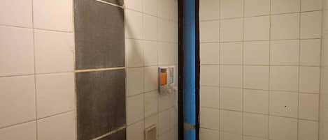 Un baño con paredes de azulejos blancos, una ducha con cabezal de ducha manual y un tubo vertical azul.
